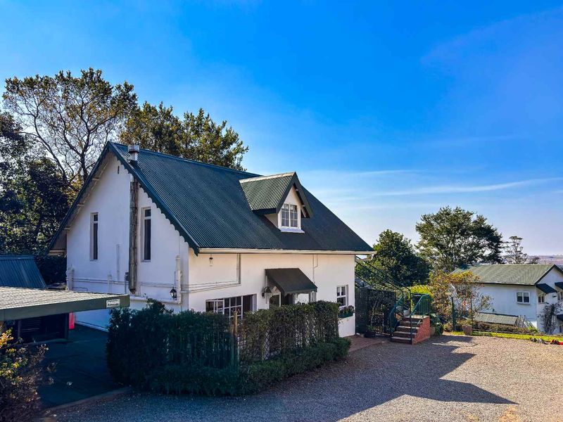 Exterior view of a charming property featuring a pitched metal roof, dormer window, attached carport, and an external staircase leading to the upper level.