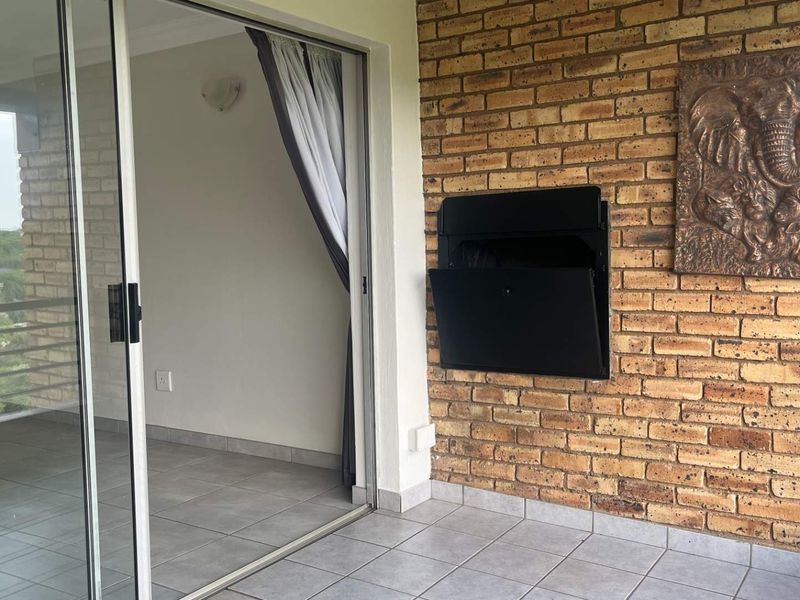 A covered balcony featuring tiled flooring, an exposed brick wall, and a built-in braai, providing a seamless transition to the interior living space.