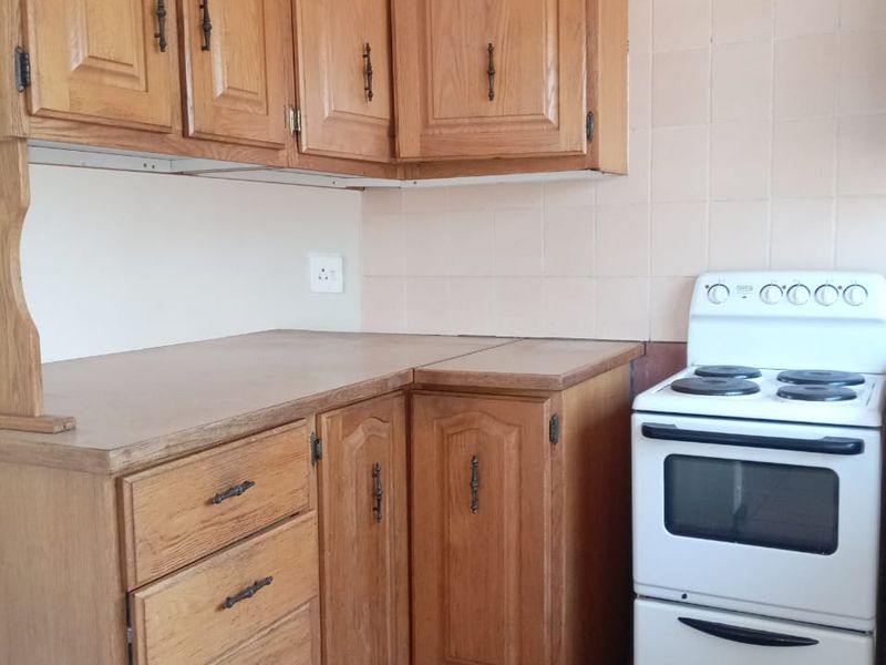 A dated kitchen featuring wooden cabinetry, tiled backsplash, and tiled flooring, equipped with a freestanding electric stove.