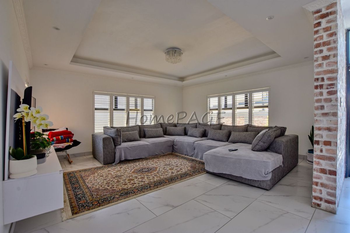 Spacious living room featuring a tray ceiling, recessed lighting, modern tiled flooring, and a decorative exposed brick pillar.