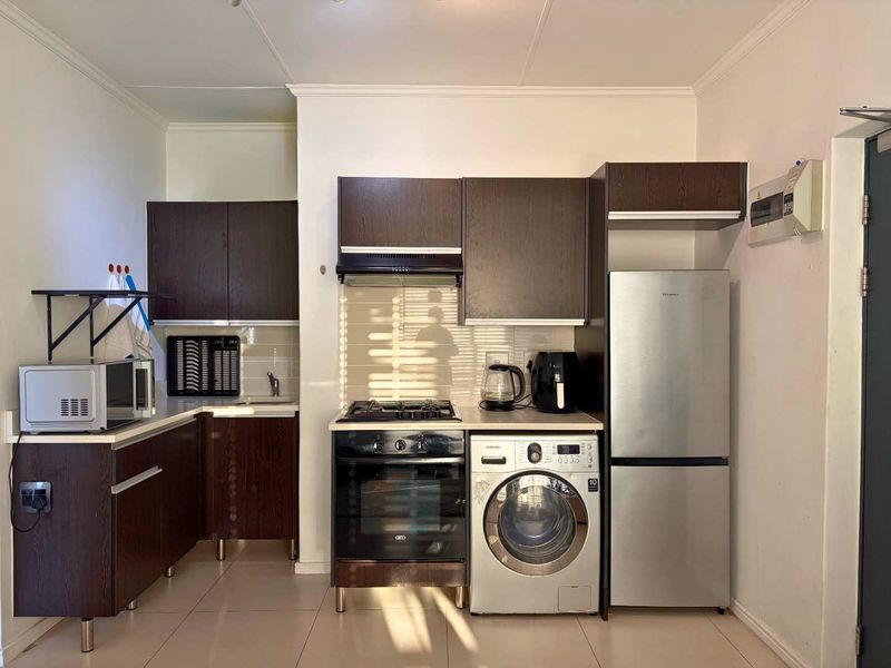 Compact kitchen featuring dark wood cabinetry, built-in oven with gas hob, extractor fan, and tiled flooring with integrated appliance space.