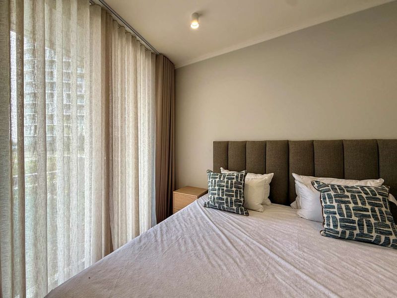A well-maintained bedroom featuring neutral tones, floor-to-ceiling curtains, and access to an outdoor area through a sliding glass door.