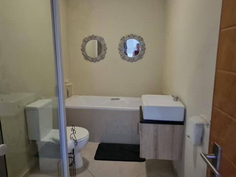 A functional bathroom featuring a shower enclosure, bathtub, wall-mounted vanity, and tiled flooring, providing a clean and practical layout.
