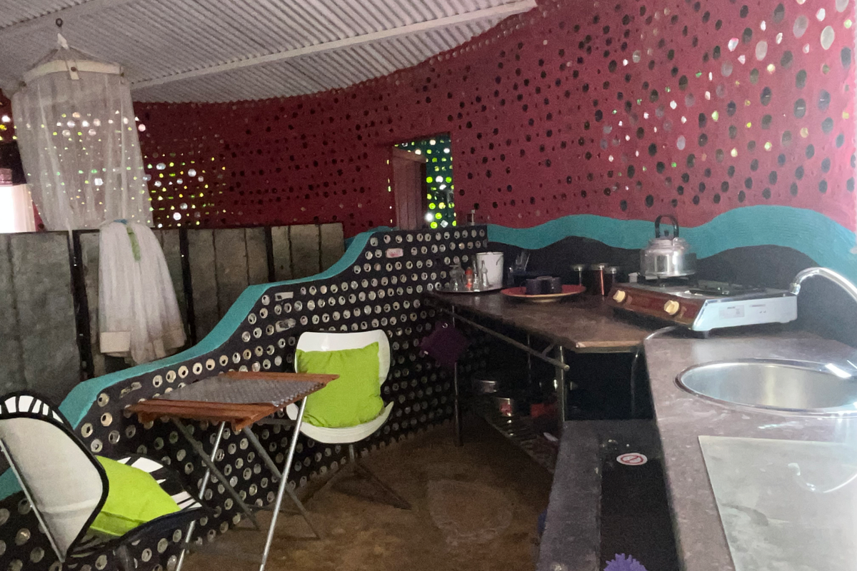 A rustic kitchen area featuring unique bottle-wall construction, a stainless steel sink, and a built-in countertop with a gas cooktop.