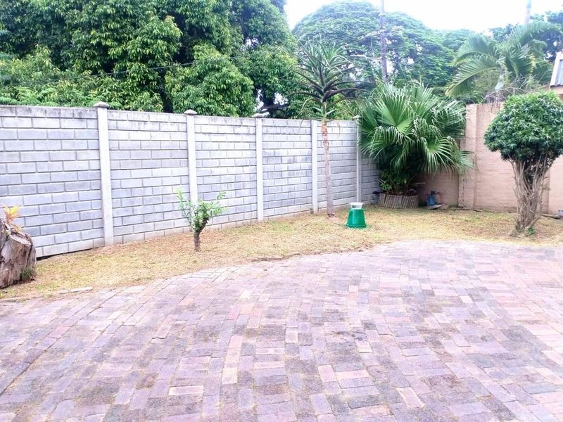A private rear garden area featuring a paved surface and a concrete block boundary wall with established trees and shrubs.