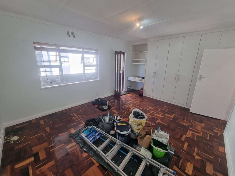 A spacious bedroom featuring classic parquet flooring, extensive built-in cupboard storage, and a convenient integrated desk area, currently undergoing minor maintenance.