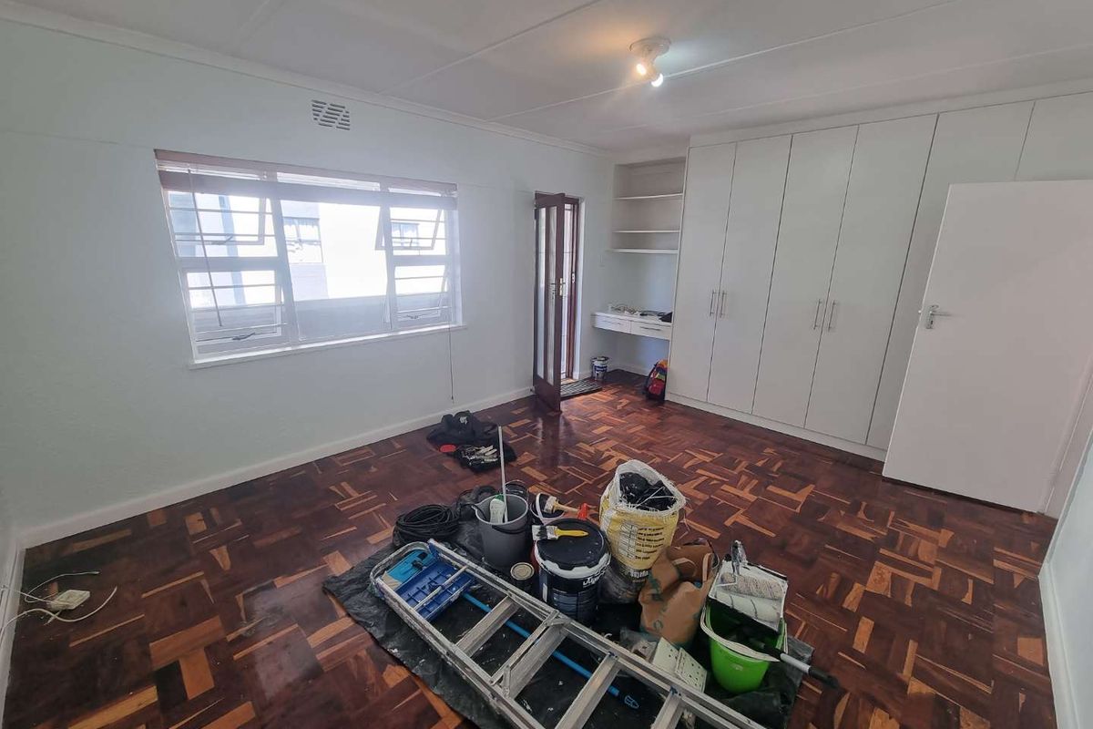 A spacious bedroom featuring classic parquet flooring, extensive built-in cupboard storage, and a convenient integrated desk area, currently undergoing minor maintenance.