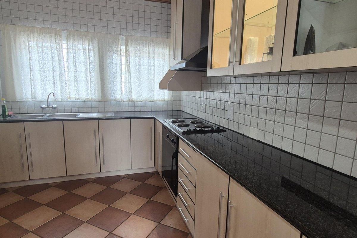 Functional kitchen featuring light wood cabinetry, dark granite countertops, built-in oven, hob, extractor fan, and double basin sink with tiled splashbacks.