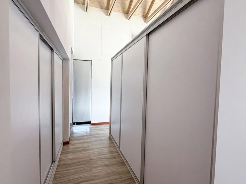 A bright hallway featuring modern built-in cupboards, light laminate flooring, and high ceilings with exposed timber rafters.