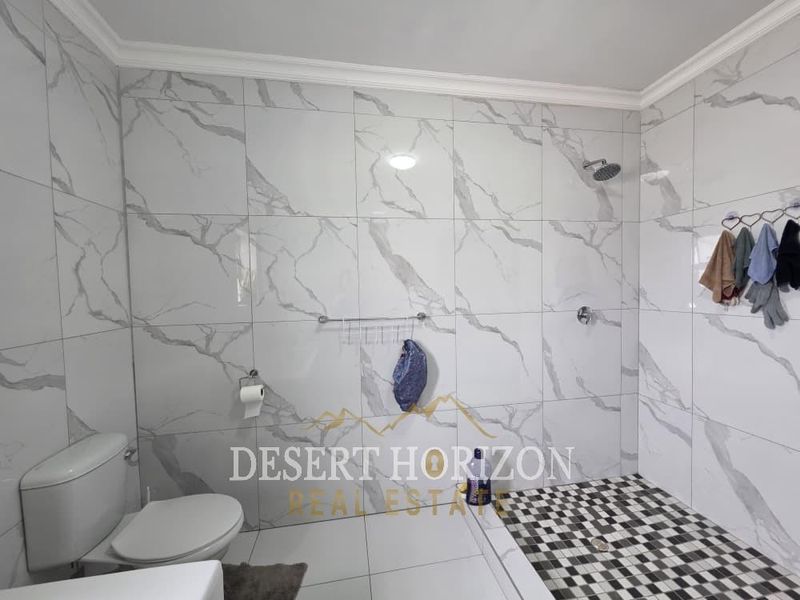 A modern bathroom featuring marble-look wall tiles, a checkered floor, and a walk-in shower area.
