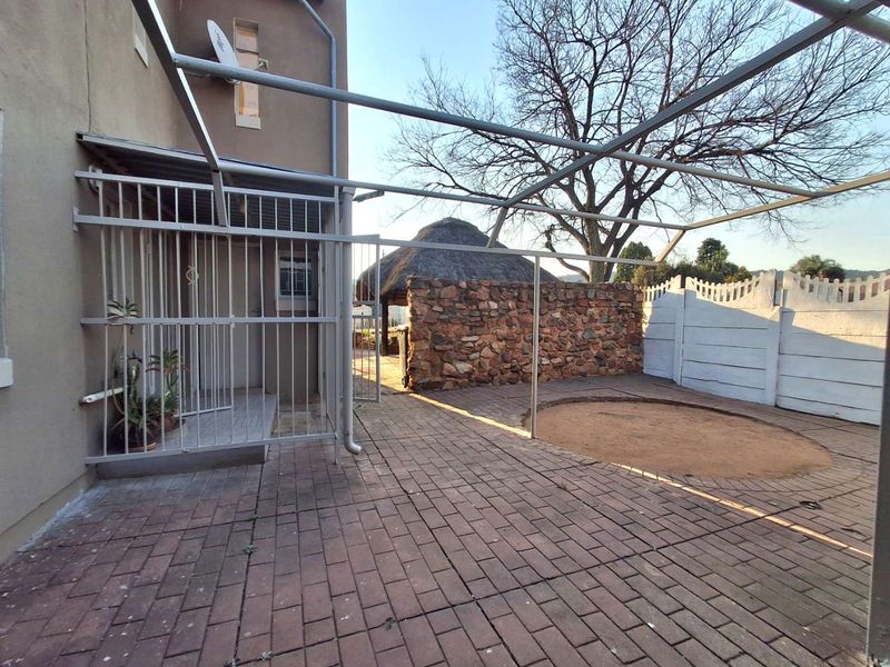 Rear exterior area featuring a paved patio, metal pergola frame, stone feature wall, and a thatched lapa in the background.