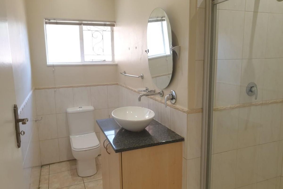 A functional bathroom featuring a shower enclosure, a vanity cabinet with a granite countertop, a vessel sink, and a toilet.
