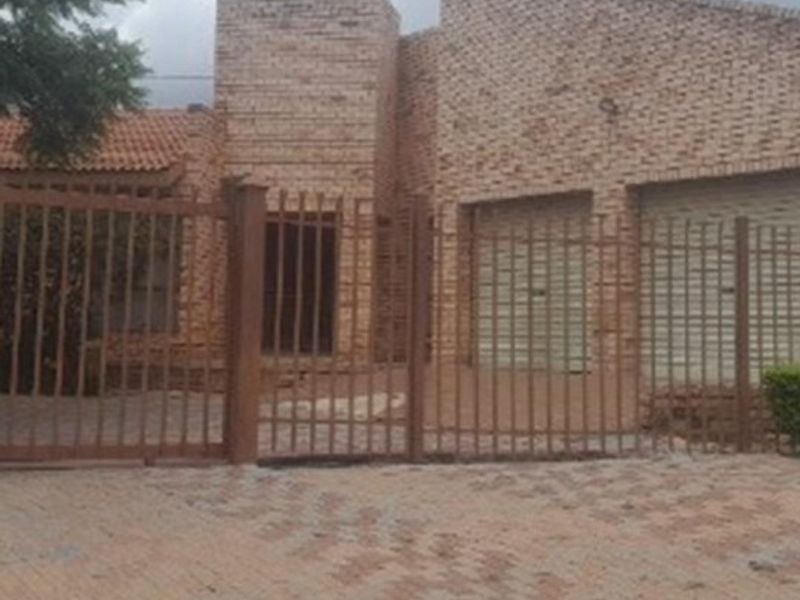 Front elevation of a face brick house featuring a double garage, paved driveway, and secure metal perimeter fencing.