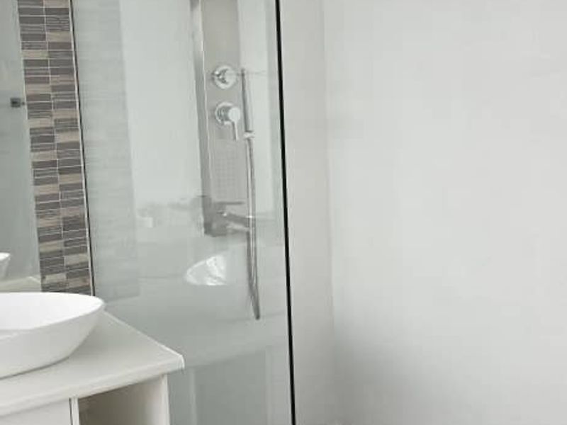 Modern bathroom featuring a glass-enclosed shower with a stainless steel shower panel, vessel sink vanity, and stylish mosaic tile accents.