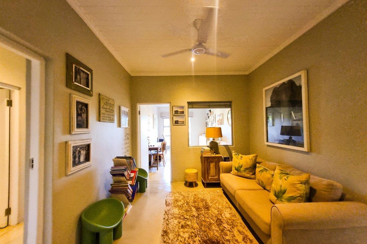 A cozy living room featuring a ceiling fan, neutral wall tones, and an interior window looking through to the adjacent dining area.