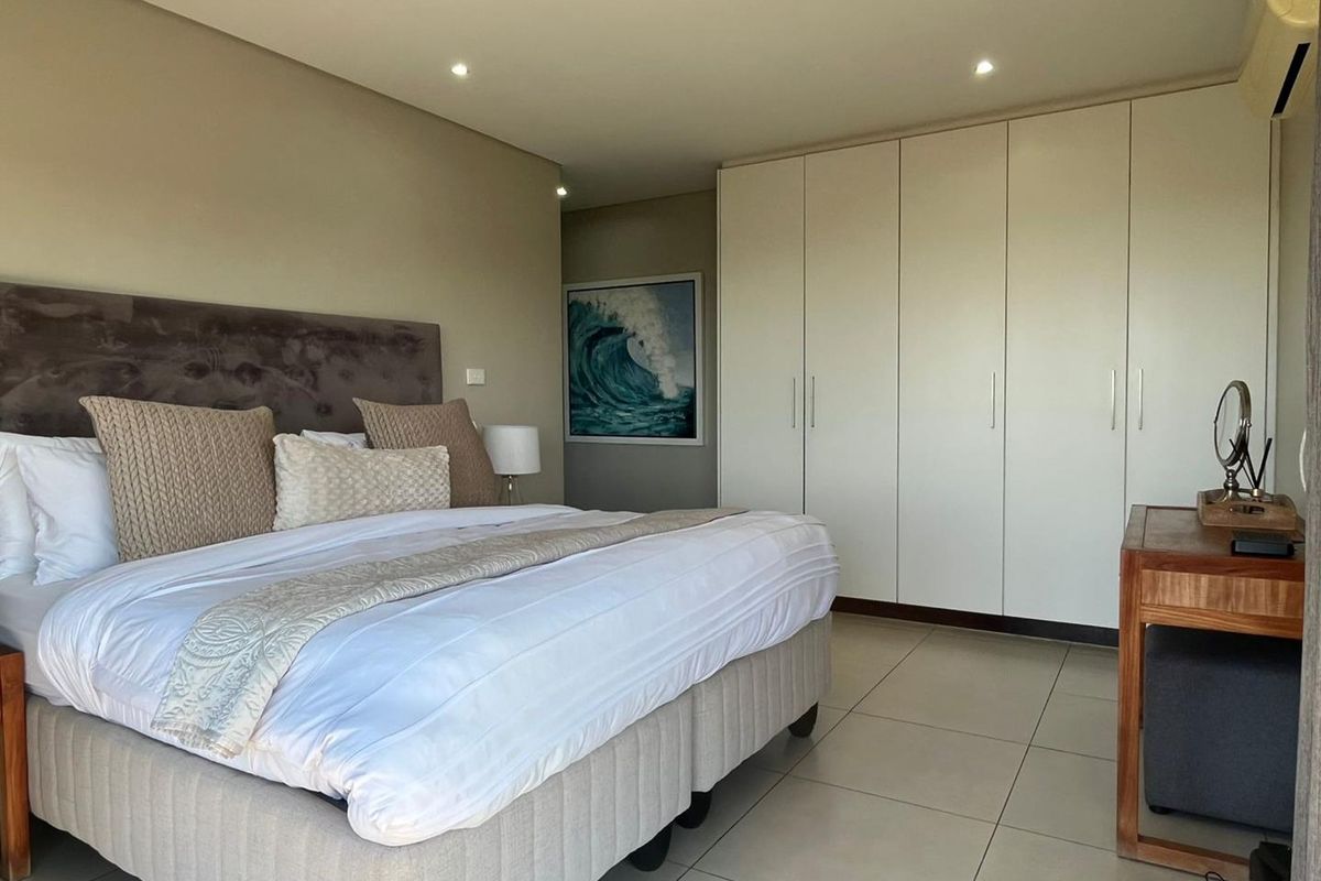 A well-maintained bedroom featuring neutral tiled flooring, recessed ceiling lighting, and extensive built-in floor-to-ceiling wardrobes providing ample storage space.