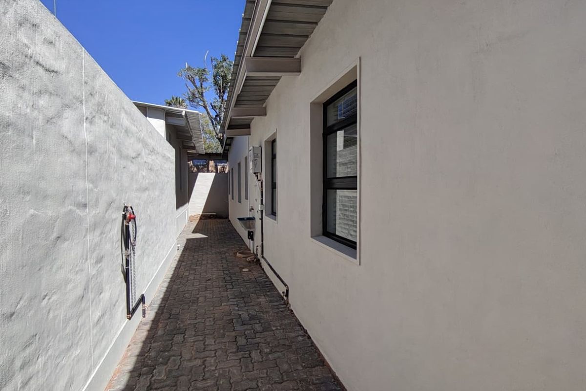 A clean side passage or rear exterior walkway featuring paved flooring, boundary walls, and functional external plumbing fixtures.