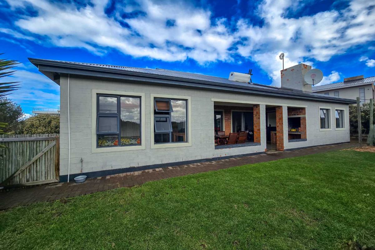 Rear view of the house featuring a covered patio area with a built-in braai, brick accents, and a well-maintained lawn.