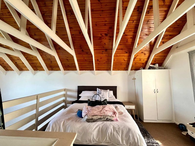 A loft-style bedroom featuring a high vaulted ceiling with exposed timber beams, a built-in wardrobe, and a mezzanine-style railing overlooking the lower level.