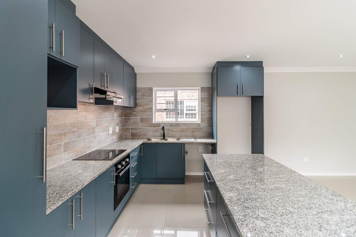 Modern kitchen featuring blue cabinetry, granite countertops, a central island, built-in oven, electric hob, and a tiled backsplash.