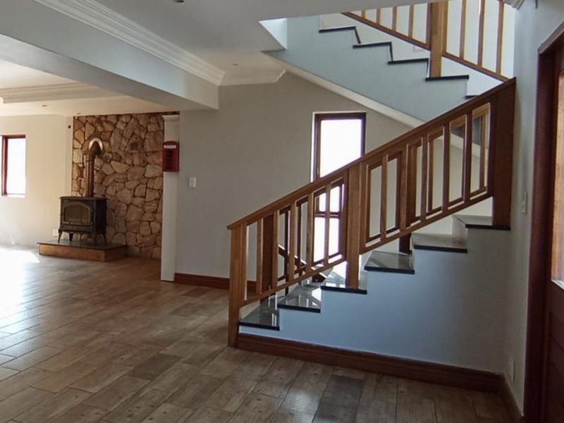 Spacious living area featuring a striking stone fireplace, timber staircase with balustrade, and modern tiled flooring throughout.