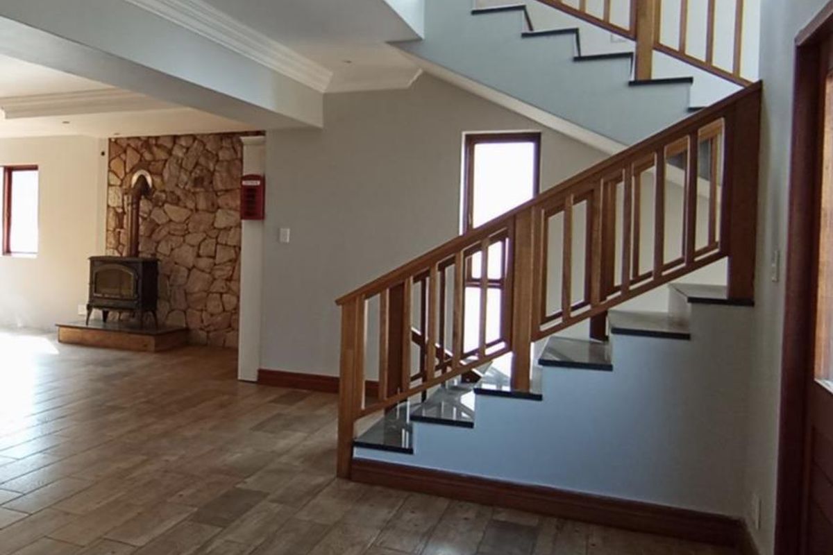 Spacious living area featuring a striking stone fireplace, timber staircase with balustrade, and modern tiled flooring throughout.