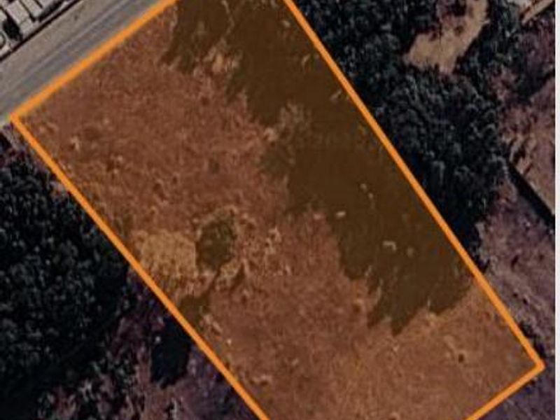 Aerial view of a vacant commercial land plot with clear boundary markings, situated near existing road infrastructure and surrounding vegetation.