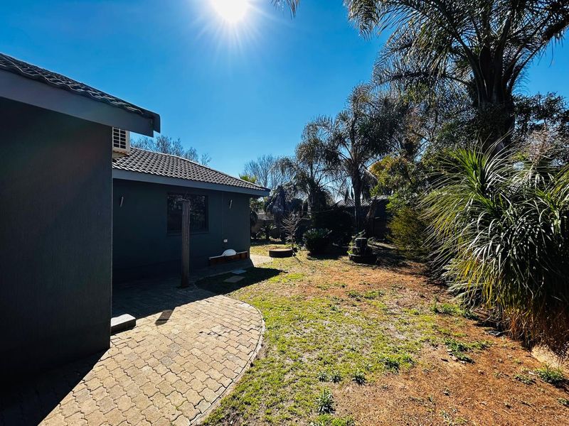Rear view of the property featuring a paved patio area, tiled roof, and a spacious garden with established trees and shrubs.