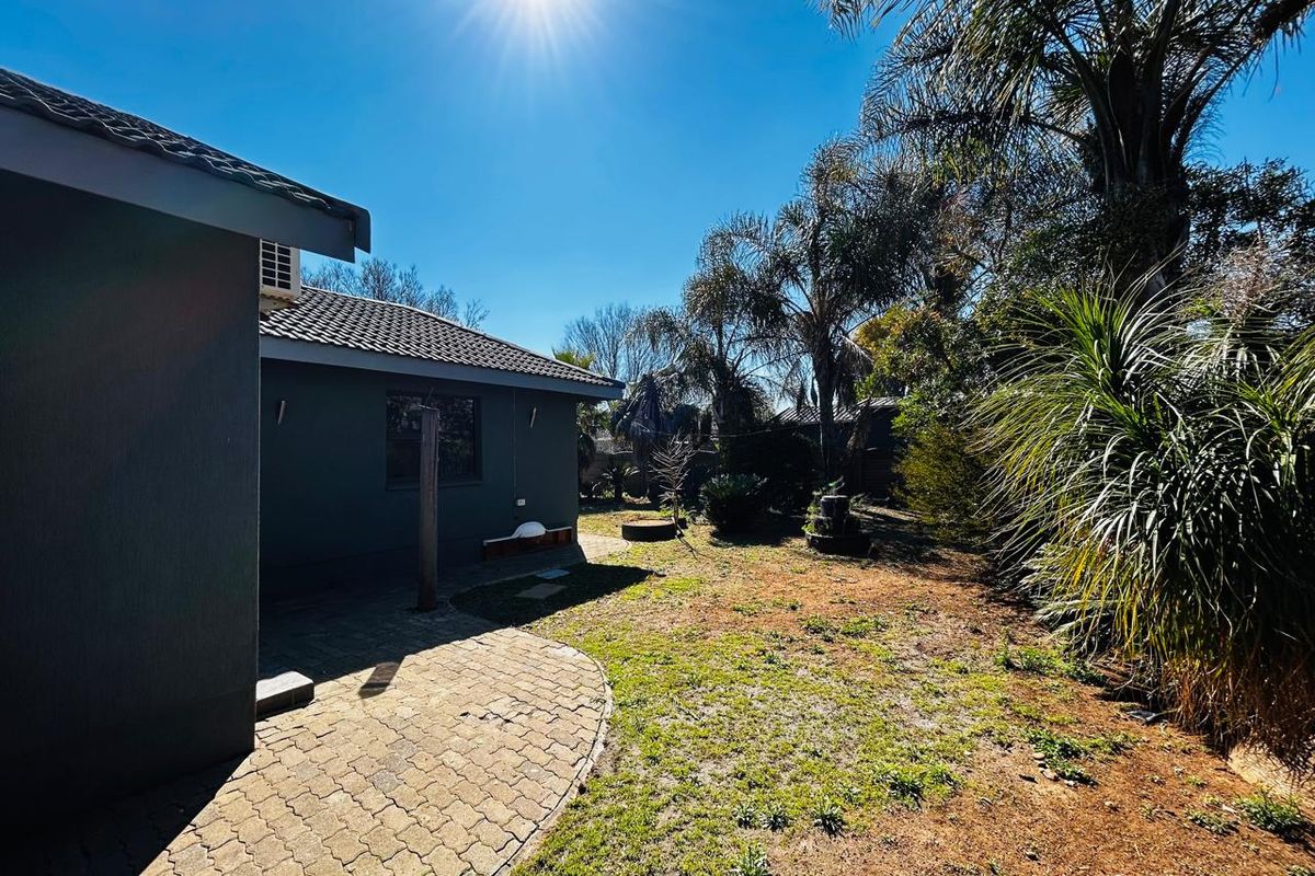 Rear view of the property featuring a paved patio area, tiled roof, and a spacious garden with established trees and shrubs.