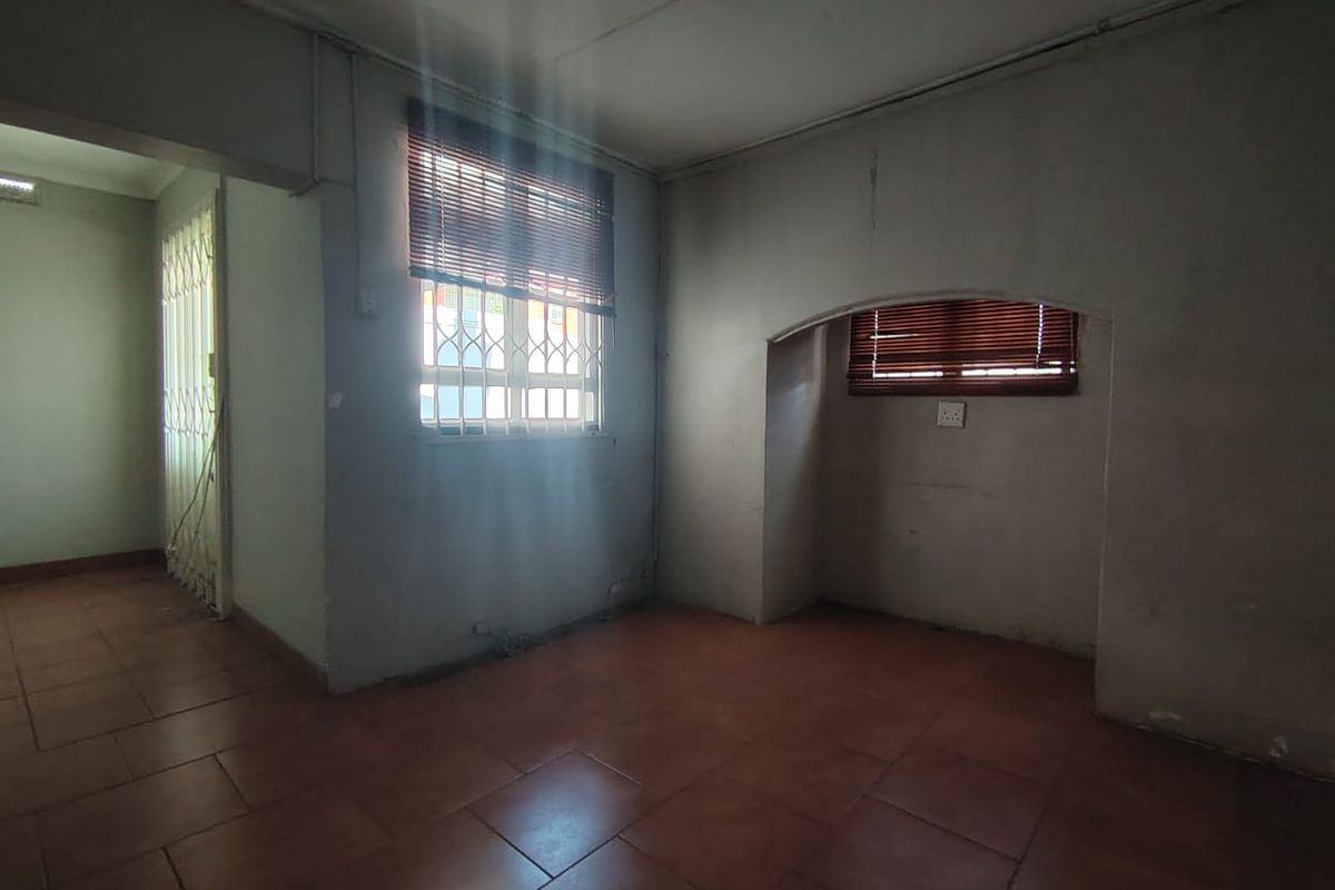 An empty office space featuring tiled flooring, security bars on windows, and neutral walls, offering a blank canvas for professional customization.