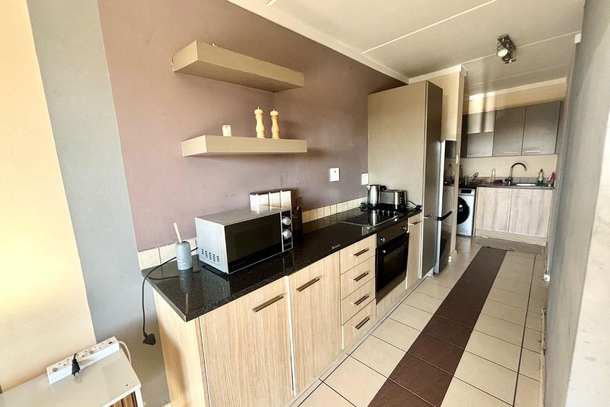 A functional galley-style kitchen featuring built-in cabinetry, granite countertops, an integrated oven and hob, and tiled flooring throughout.