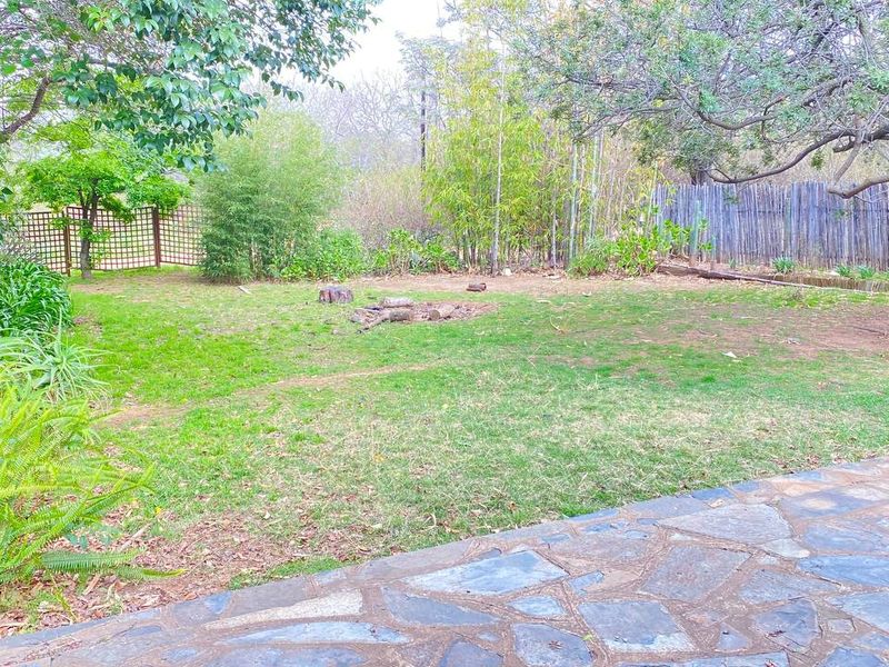 A spacious rear garden featuring a stone-paved patio area, established trees, and perimeter fencing, offering a private outdoor space for the cottage.