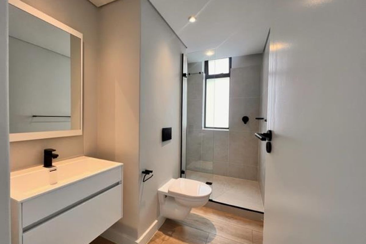 Modern bathroom featuring a wall-mounted vanity, walk-in shower with glass screen, and wall-mounted toilet with contemporary black fixtures.