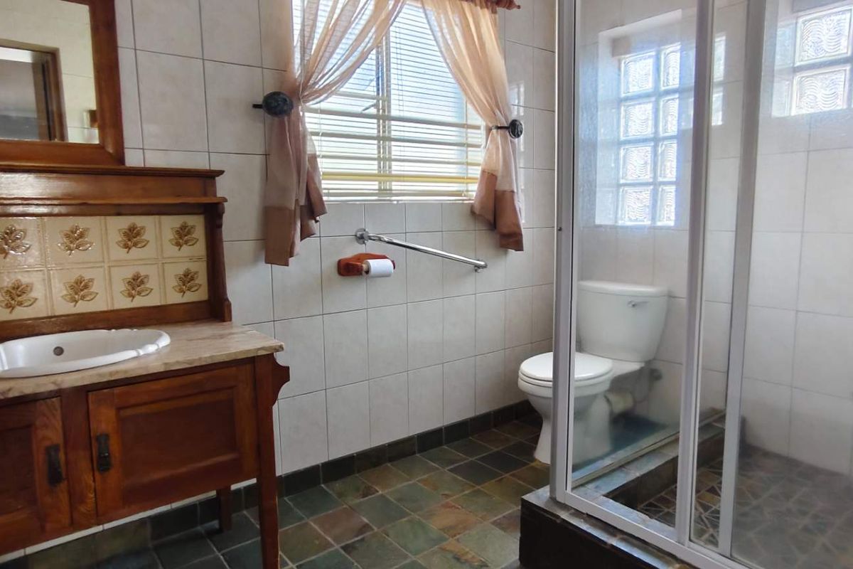 A functional bathroom featuring a wooden vanity, tiled walls, a glass-enclosed shower, and a toilet with a grab rail.