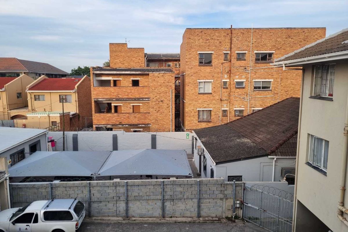 An elevated view of the apartment complex exterior, featuring brick building facades, a tiled roof, and a secure perimeter wall with carport parking.