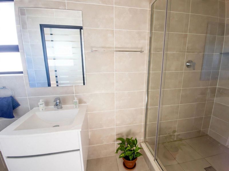 Modern bathroom featuring a white vanity cabinet, glass-enclosed shower, neutral ceramic wall and floor tiles, and a wall-mounted mirror.