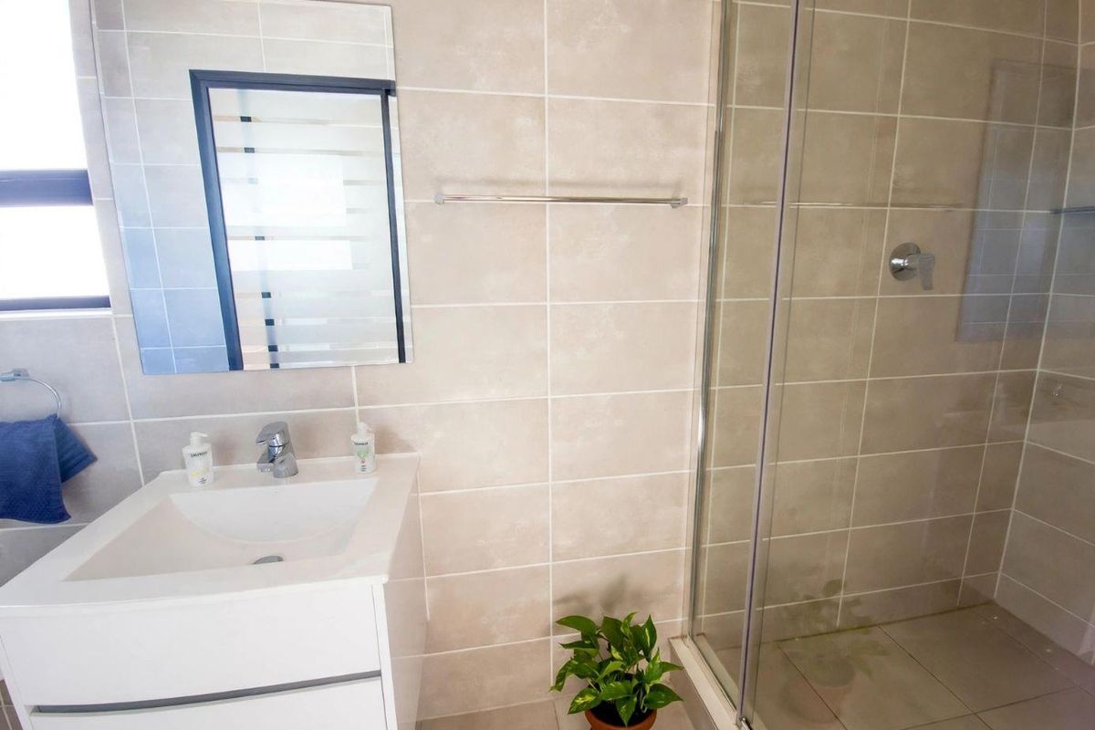 Modern bathroom featuring a white vanity cabinet, glass-enclosed shower, neutral ceramic wall and floor tiles, and a wall-mounted mirror.