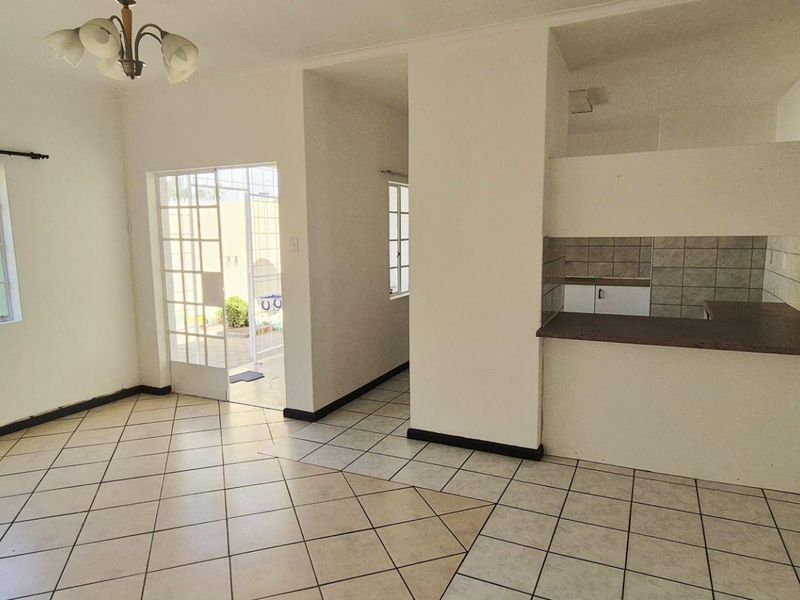 Open plan living and kitchen area featuring tiled flooring, a breakfast bar, and direct access to the outdoor space through a glass paneled door.