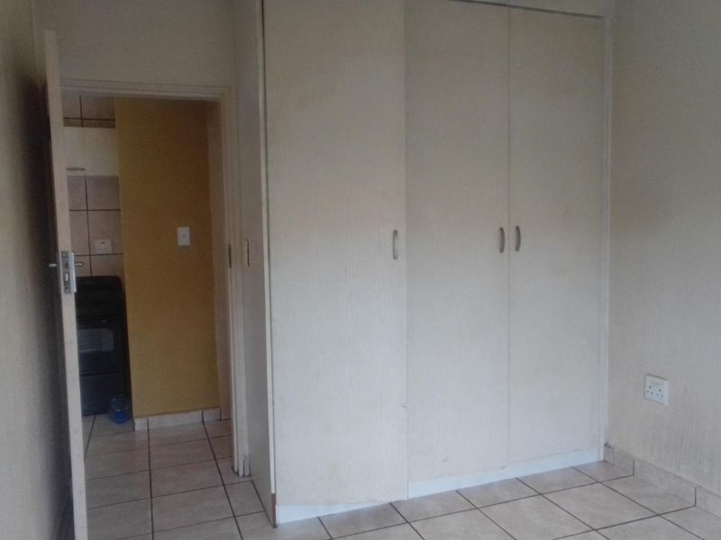 A bedroom featuring built-in cupboards and tiled flooring, with a view into an adjacent kitchen area.