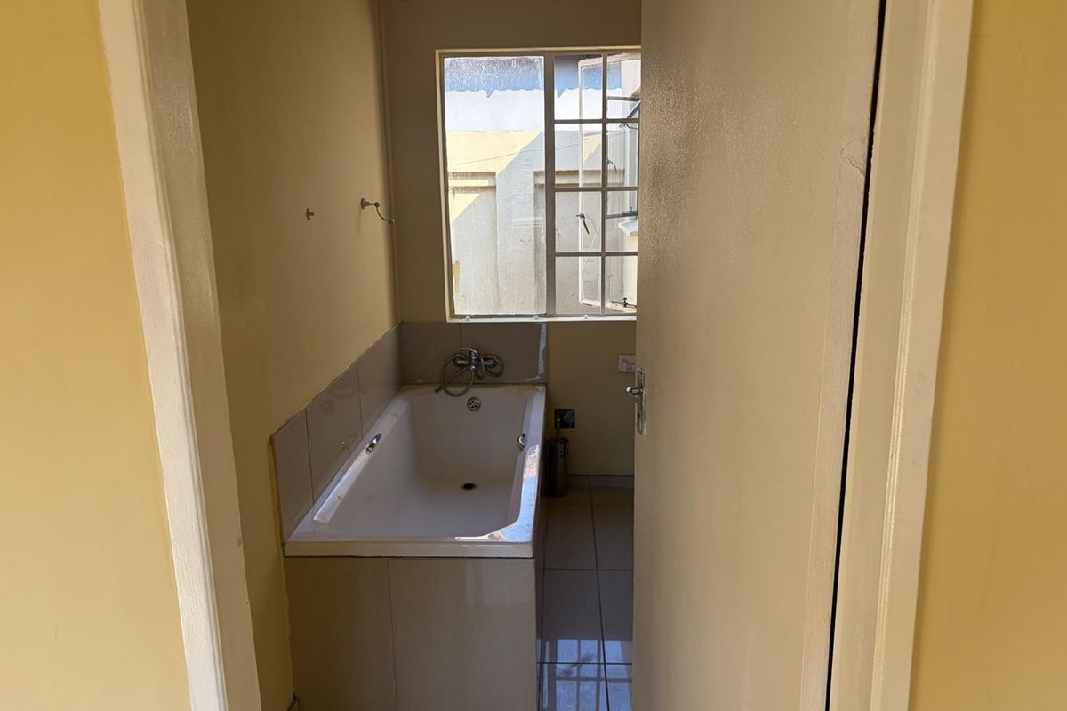 A compact bathroom featuring a built-in bathtub with tiled splashback and tiled flooring, requiring cosmetic updates to improve its overall condition.