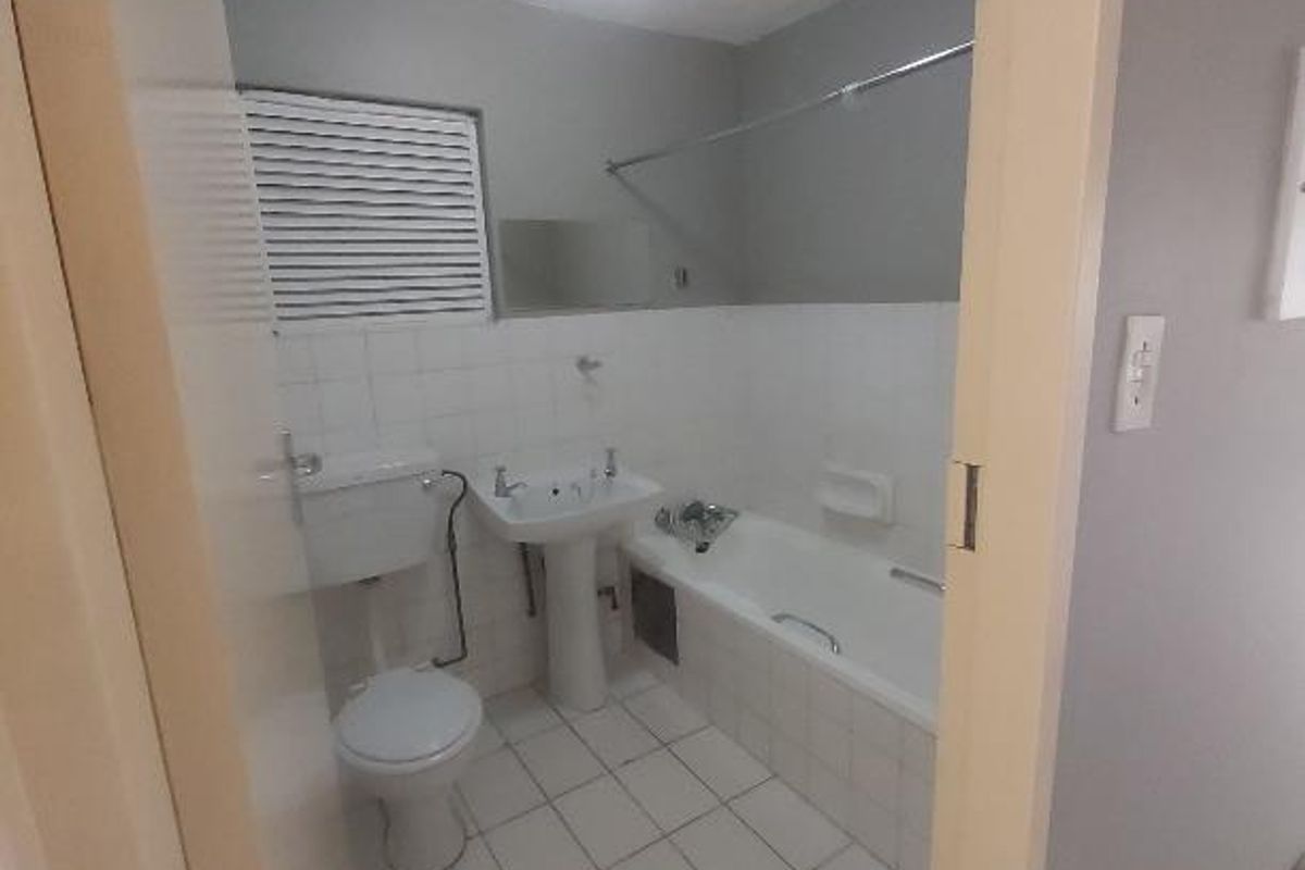 A functional bathroom featuring a pedestal basin, toilet, and a bathtub with a shower rail, finished with white wall and floor tiling.