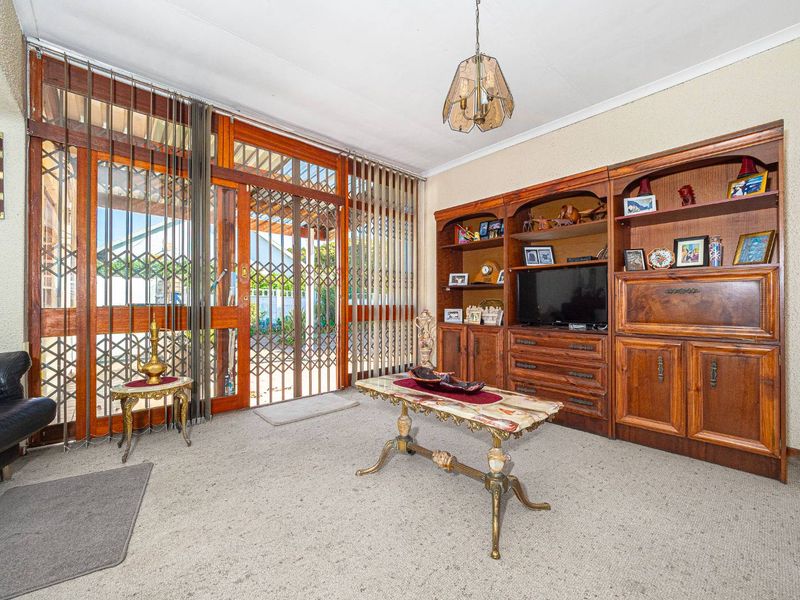 A living room featuring timber-framed glass doors with security gates, built-in wooden cabinetry, and carpet flooring, offering potential for modernization.