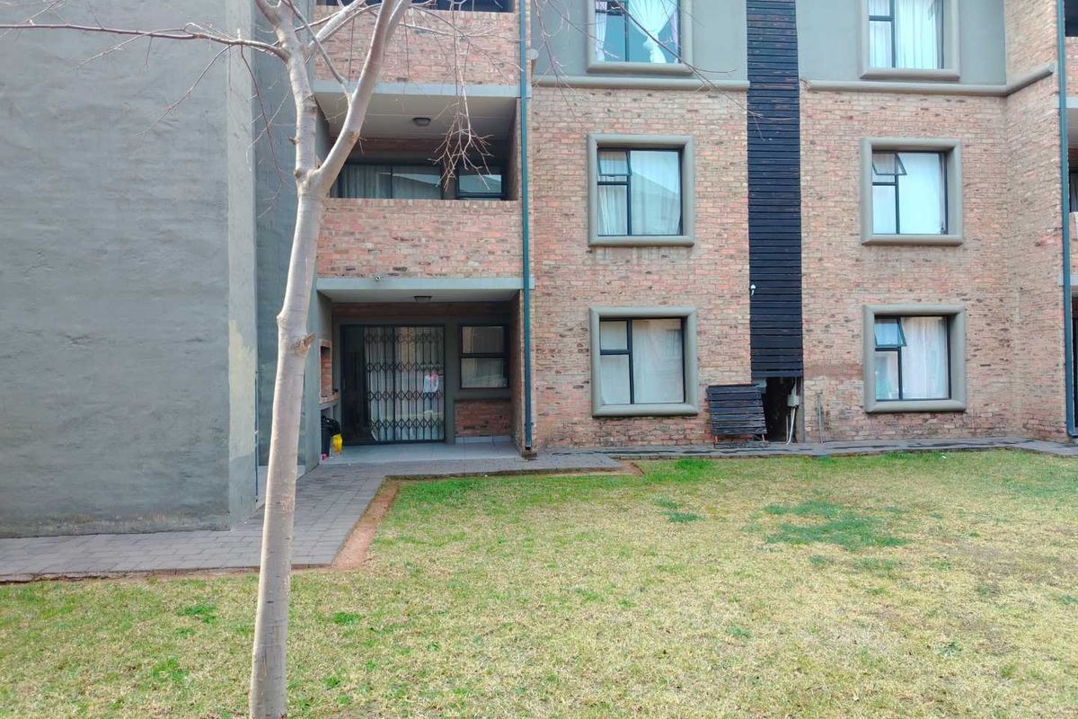 Rear view of an apartment building featuring exposed brick facade, ground floor patio with security gate, and a shared garden area.