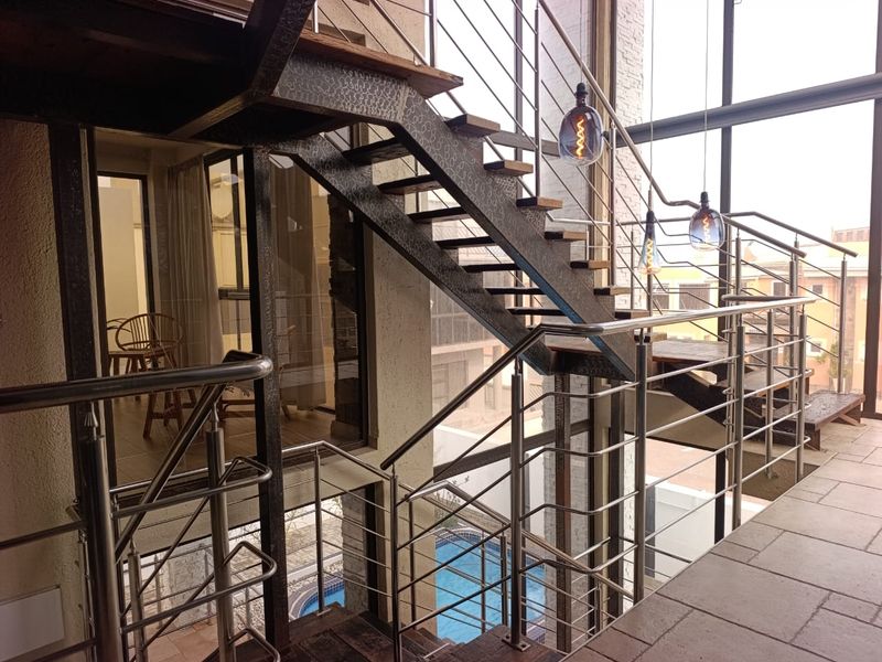 Modern industrial-style staircase featuring a metal frame, stainless steel balustrades, and expansive floor-to-ceiling windows overlooking the pool area.