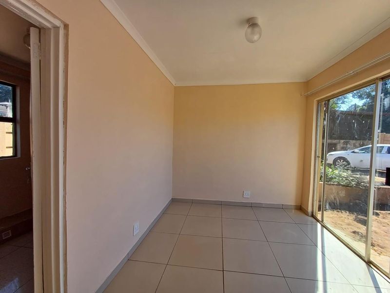 A bright, empty living area featuring neutral tiled flooring, cove cornicing, and a large sliding glass door providing natural light and garden access.