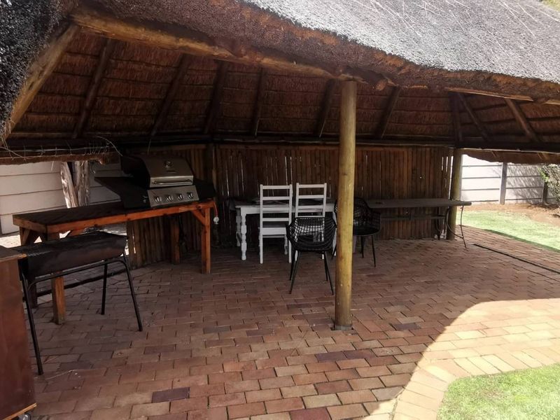 Covered outdoor entertainment area featuring a traditional thatch roof, timber support posts, and brick paving, ideal for alfresco dining and social gatherings.