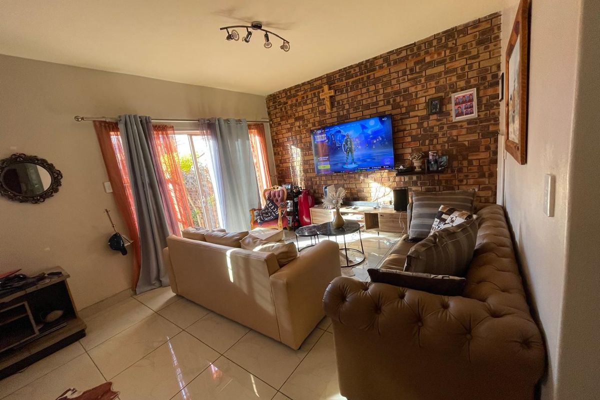 A cozy living room featuring a prominent exposed brick feature wall, tiled flooring, and sliding glass doors providing access to the outdoor area.