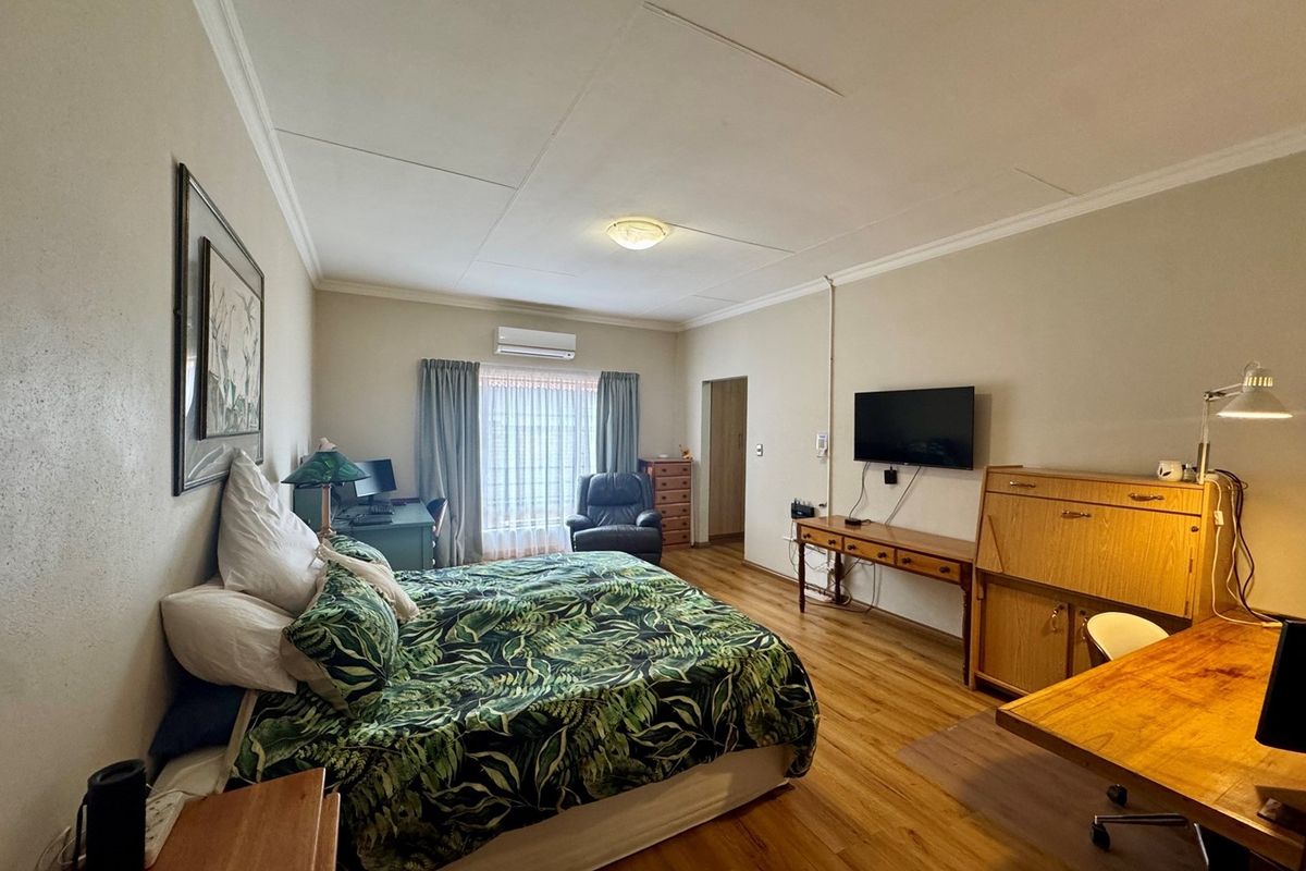 Spacious bedroom featuring laminate flooring, coving, and a wall-mounted split-system air conditioner, offering a functional and comfortable living space.