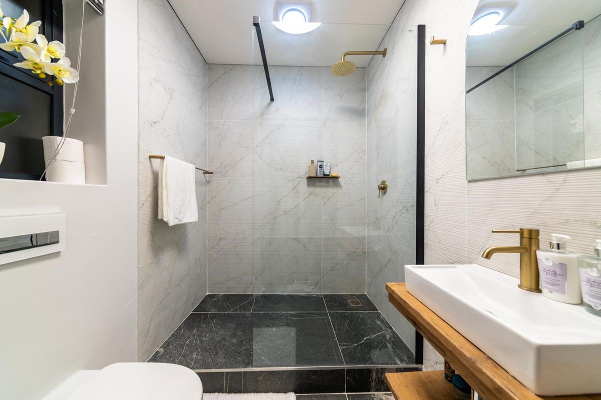 Modern bathroom featuring a walk-in shower with marble-look wall tiles, dark stone floor tiles, gold fixtures, and a floating timber vanity.