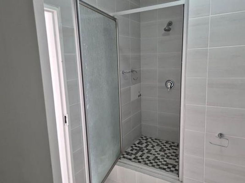 A clean, modern bathroom shower featuring light grey wall tiles, a mosaic-tiled shower floor, and a glass-enclosed shower unit.